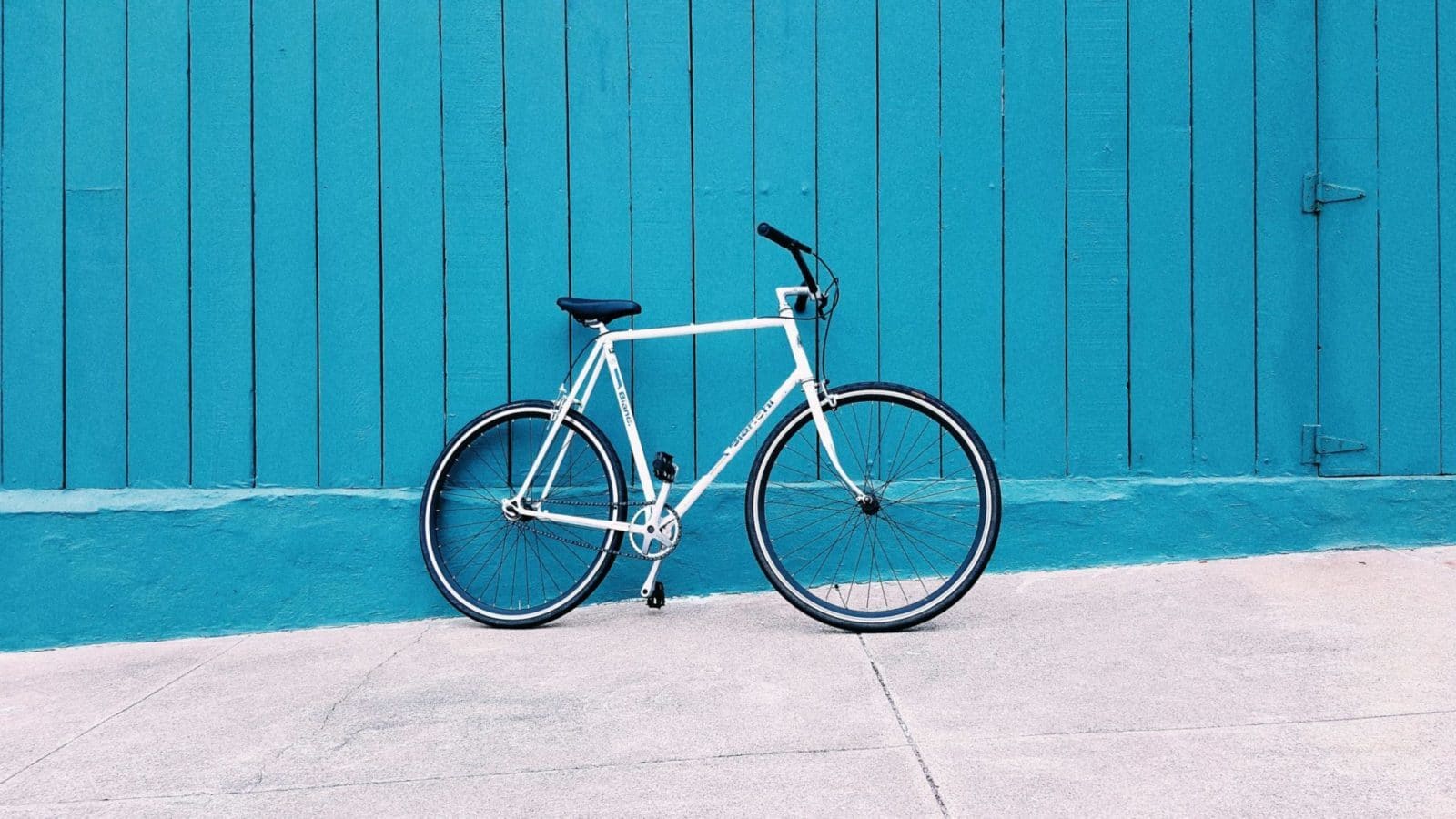 white road bike leaning on teal wooden wall during daytime